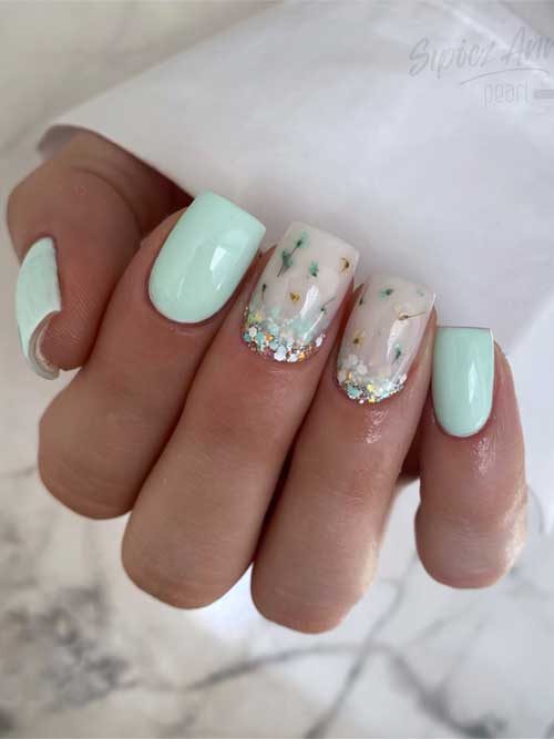 Pastel spring nails with mint green on three fingers and nude floral designs on two, accented with glittery tips.