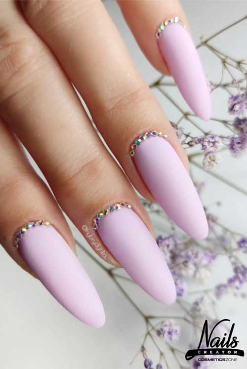 Soft pastel lavender nails with a matte finish, adorned with multicolored rhinestones for a fresh, delicate look.